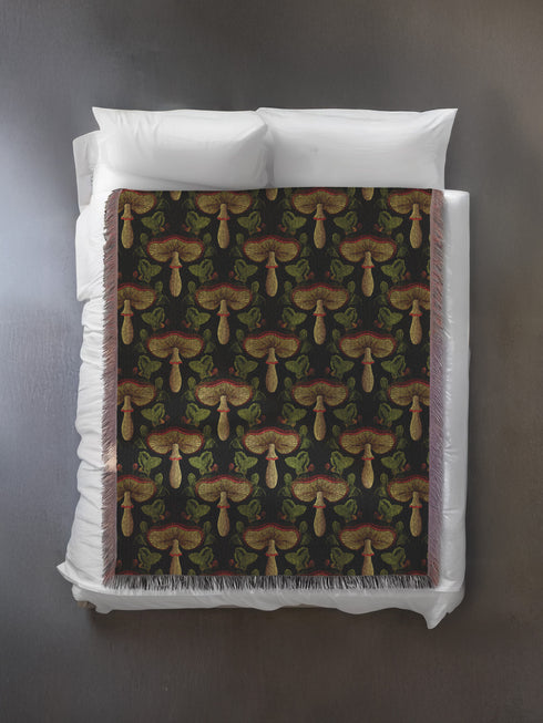 A woven cotton throw featuring an intricate mushroom and foliage pattern in deep charcoal and golden hues, framed by soft fringe.